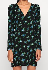 Robe fleurie noire à manches longues, avec un décolleté en V profond. Le design comprend des roses bleues et des feuilles vertes sur un tissu texturé.