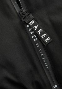 Čierny materiál so viditeľným zipsom obsahuje štítok s nápisom "BAKER by Ted Baker", čo zdôrazňuje štýlový a moderný dizajn.