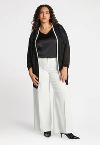 Sort strikket cardigan med sølvakcenter, parret med en sort satin top og hvide brede bukser. Sorte spidse hæle fuldender looket.