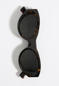 Gafas de sol estilo ojo de gato con un marco de carey brillante, lentes oscuros y bordes gruesos y curvados. Patrón intrincado en el material del marco.