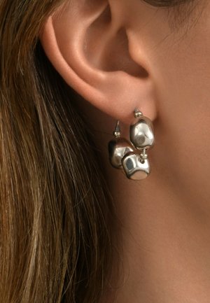 Boucles d'oreilles en argent comportant trois éléments de forme irrégulière, polis avec une surface réfléchissante, attachés par de petites perles métalliques à des crochets.