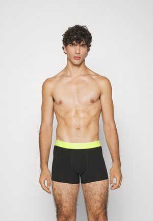 Bóxer negro con una cinturilla de color amarillo neón que presenta el texto "LACOSTE". El material parece suave y ajustado, diseñado para la comodidad.