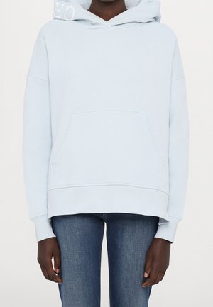 Lichtblauwe hooded sweatshirt met een voorzak, oversized ontwerp, geribde manchetten en een subtiel logo op de capuchon. In combinatie met denim jeans.