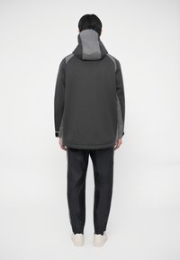 Grå huva jacka med en texturerad finish och kontrasterande paneler, ihop med svarta byxor med vita sidränder och elastiska manschetter.