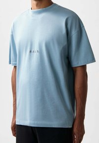 Helles blaues T-Shirt mit kurzen Ärmeln aus weichem Baumwollstoff, das einen lässigen Schnitt und ein dezentes gesticktes Logo auf der Brust aufweist.