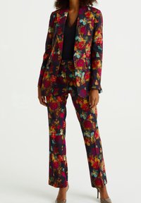 Květinový oblek s tmavým pozadím a vícebarevnými květy v červené, růžové a tyrkysové barvě. Střih na míru se zahrnuje kalhoty a odpovídající sako.