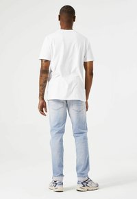 Camiseta de algodón blanca de manga corta, combinada con unos vaqueros de denim azul claro y zapatillas grises con acentos azules. Diseño sencillo, sin patrones.