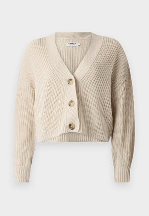 Beige kort cardigan med V-ringning, ribbat mönster, långa ärmar och fyra stora knappar framtill. Tillverkad av stickat tyg.