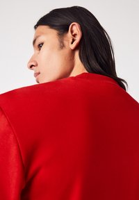 Sweatshirt rouge à col rond en coton, présentant une texture lisse et une coupe ajustée. L'encolure arrière affiche un détail discret de couture.