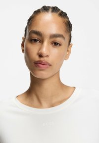 Biała bawełniana koszulka z okrągłym dekoltem i subtelnym logo "BOSS" na środku. Gładka tekstura, krótkie rękawy i luźny krój.