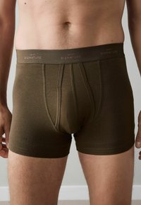 Barna pamutkeverék boxeralsó rugalmas derékpánttal, amelyen a "NEXT SIGNATURE" logó látható. Simaszövet, testhezálló szabás, combközépig érő hossz.