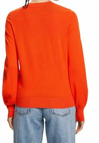 Personne portant un pull à manches longues orange vif et un jean en denim bleu clair, vue de dos.