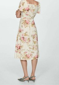 Robe midi florale avec décolleté carré, manches courtes à volants et taille cintrée. Présente un fond crème avec des motifs floraux roses et verts.