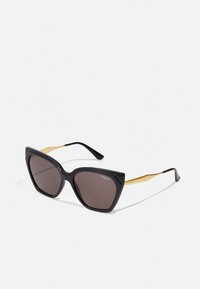 Lunettes de soleil cat-eye noires avec des verres sombres, monture en plastique verni et accents en métal doré sur les branches, arborant la marque "vogue".