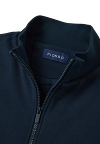 Giacca zip-up blu navy con colletto alto, polsini a coste e etichetta con marchio "PIOMBO". Il tessuto sembra morbido e con una texture lavorata.