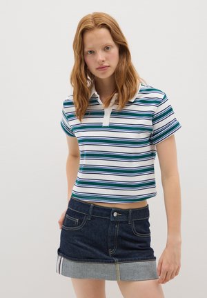 Polo a maniche corte con righe orizzontali verdi e blu navy su sfondo bianco; presenta un colletto e una chiusura a bottoni. Abbinato a una mini gonna in denim con orlo azzurro chiaro.