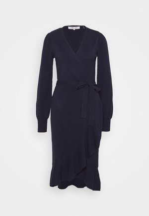 Robe portefeuille en maille bleu marine à manches longues avec décolleté en V, ceinture à la taille et ourlet asymétrique à volants.