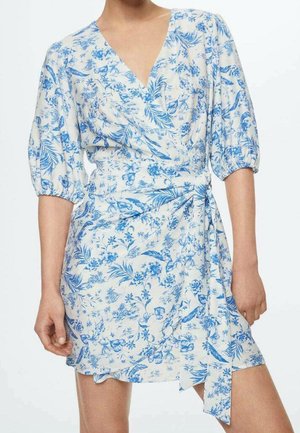 Weißes Wickelkleid mit blauem Blumen- und Blattmuster, V-Ausschnitt, gepuffte Ellbogenlange Ärmel und gebundener Taillengürtel an einer stehenden Person.