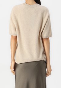 Pull en cachemire beige à manches courtes, col rond et coupe décontractée. Présente une texture subtile et une bordure côtelée le long des bords.