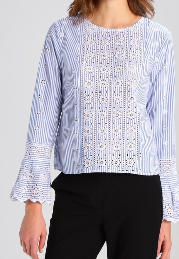 Blouse rayée bleue et blanche avec des détails découpés brodés, manches évasées trois-quarts et encolure arrondie. Tissu en coton.
