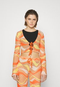 Top cropped e calças combinando em tricot texturizado nas cores laranja, amarelo e branco. O top apresenta um decote em V profundo e um fechamento frontal com laço.