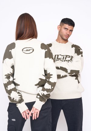 Sweater i creme med olivengrønne camoærmer. Ribbet manchetter og kant. Har branding på ryggen og fronten. Sammen med sorte bukser.
