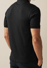 Polo noir avec un col structuré et des manches courtes, doté d'accents texturés aux ourlets des manches et d'une surface lisse.