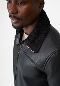 Black leather jacket with a textured black shearling collar and silver hardware, featuring a zip closure and sleek design.