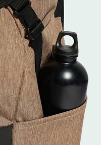 Brauner Stoff-Rucksack mit strukturierter Oberfläche, ausgestattet mit einer schwarzen Metall-Wasserflasche in einer Seitentasche und einem schwarzen verstellbaren Tragegurt.