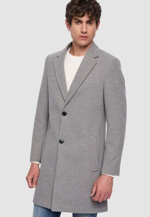 Cappotto grigio a spina di pesce con colletto a risvolto, chiusura con due bottoni, tasche laterali e texture liscia, indossato sopra a un maglione leggero.