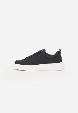 Baskets basses noires avec lacets et semelle blanche épaisse, présentées de profil sur un fond clair uni.