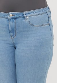 Vaqueros de denim azul claro con un diseño clásico de cinco bolsillos, acentos de costura y un cierre de botón en el frente. Textura suave, ajuste slim.