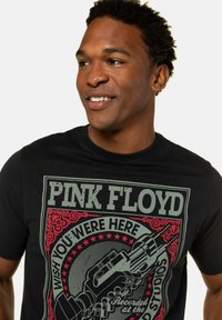 Sort bomulds t-shirt med en Pink Floyd grafisk tryk i grå og rød, med vintage-stil tekst og en detaljeret illustration af en guitar.