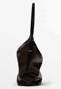 Sac à bandoulière en cuir marron foncé avec une longue sangle noire réglable et une boucle en argent, se tenant debout sur un fond blanc.