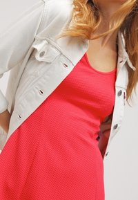 Robe rose texturée avec un col rond, superposée sous une veste en denim blanche avec fermetures à boutons et manches retroussées.