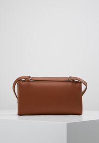 Ruskean nahkalaukku, jossa on suorakulmainen muoto, lyhyt kahva ja minimalistinen muotoilu. Sujuva pinta, ei näkyviä kuvioita.