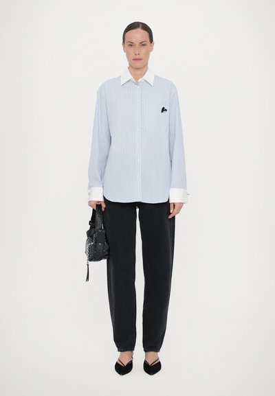 Blue and white striped button-up shirt with a white collar, oversized fit, left chest pocket, paired with black straight-leg pants and shoes.