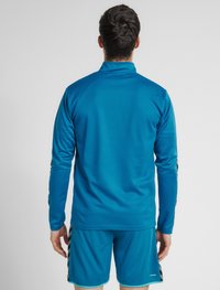Blå långärmad träningsskjorta med texturerad yta och hög krage, tillsammans med matchande blå shorts med svarta sidostråk.