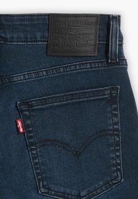 Tummansiniset farkut, joissa on takatasku ja Levi'sin punainen lappu sekä musta nahkainen Levi's-brändin läpyskä vyötäröllä.
