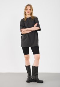 T-shirt nero oversize con maniche corte, abbinato a pantaloni ciclistici neri a coste. Modello che indossa stivali neri al ginocchio con hardware decorativo.