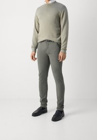 Felpa grigia e pantaloni slim-fit verde oliva abbinati a scarpe slip-on nere, con tessuti lisci e minimalismo nei dettagli.