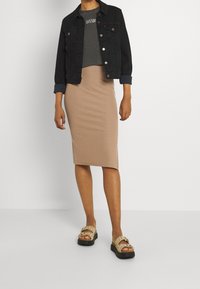 Veste en denim noire avec boutons argentés, t-shirt gris court, jupe midi beige côtelée et sandales beiges avec boucles et clous.