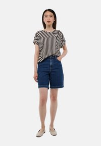 Haut à manches courtes rayé noir et crème, associé à un short en denim bleu. La tenue présente une coupe décontractée et un ourlet retroussé sur le short.