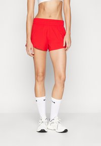 Pantaloni sportivi rossi con vita elasticizzata, caratterizzati da una superficie liscia. Abbinati a calzini bianchi Nike e scarpe da ginnastica chiare.