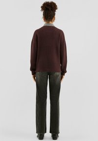 Bordowy sweter dziergany o prążkowanej fakturze, z długimi rękawami i luźnym krojem, zestawiony z ciemnymi jeansami o prostych nogawkach i czarnymi butami.