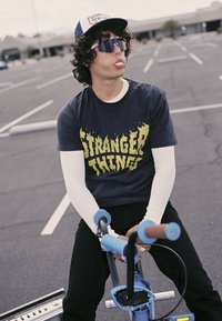 Sininen ja musta BMX-polkupyörä ruskeilla kahvoilla, jota käyttää mustaa t-paitaa, jossa on keltainen teksti, ja valkoista pitkähihnaista aluspaidan käyttäjä.