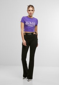 Violeta īsā T-kreklā ar baltu "Von Dutch Originals"logo; melnas sānu izteiksmīgas bikses ar aukliņu viduklī; sudraba smailējo pēdu zābaki.