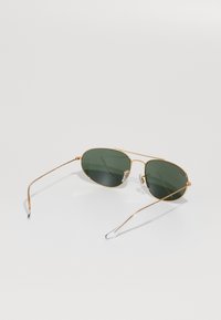 Occhiali da sole aviator in metallo dorato con lenti verde scuro. Presentano una sottile montatura in filo, cuscinetti nasali in gomma trasparente e punte delle tempie arcuate.