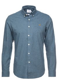 Ljusblå skjorta med knappar tillverkad av texturerad tyg. Har en smal passform, krage och en liten broderad logotyp på bröstet. Sju knappar synliga.