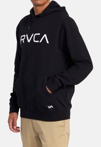 Black hoodie with front pocket, features white "RVCA" logo and "VA" accent. Made of soft fabric, designed with a drawstring hood.